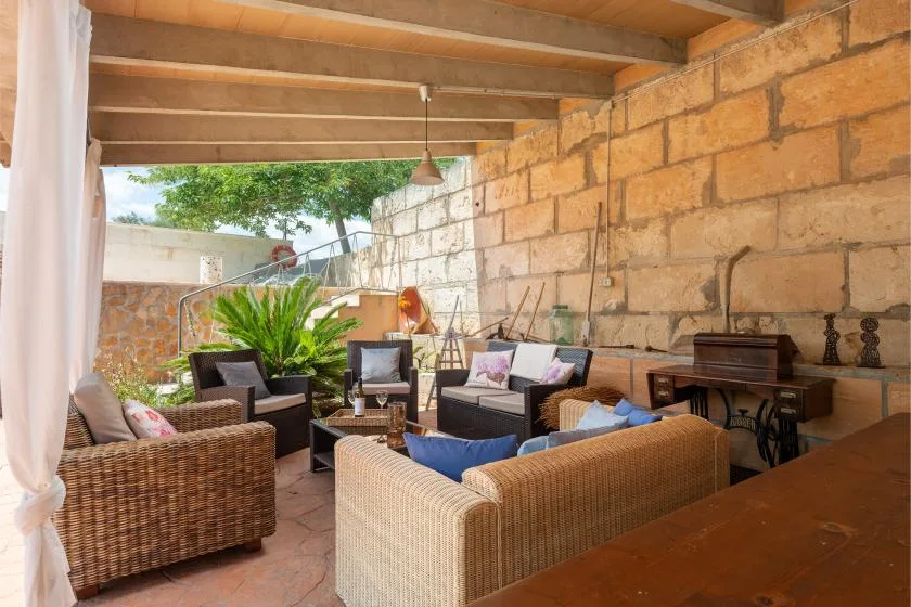 Una zona de estar exterior cubierta, con muebles de fibras tejidas y una pared de piedra.