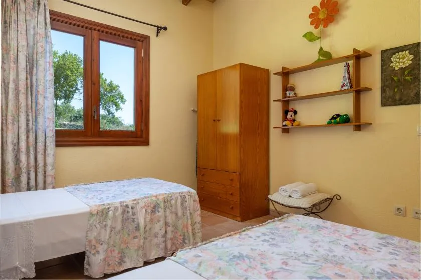 Un dormitorio con dos camas, un armario de madera y una ventana con vistas a árboles.
