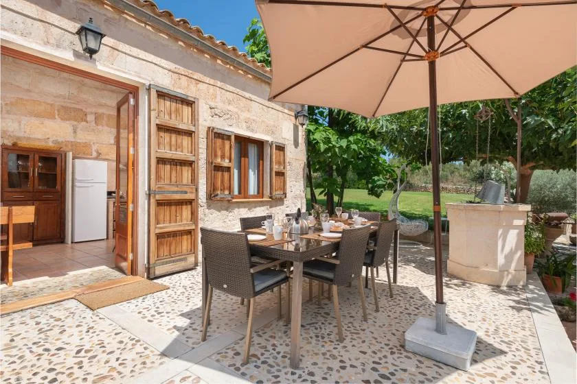 Una zona de comedor en un patio de piedra con asientos al aire libre bajo una sombrilla grande.
