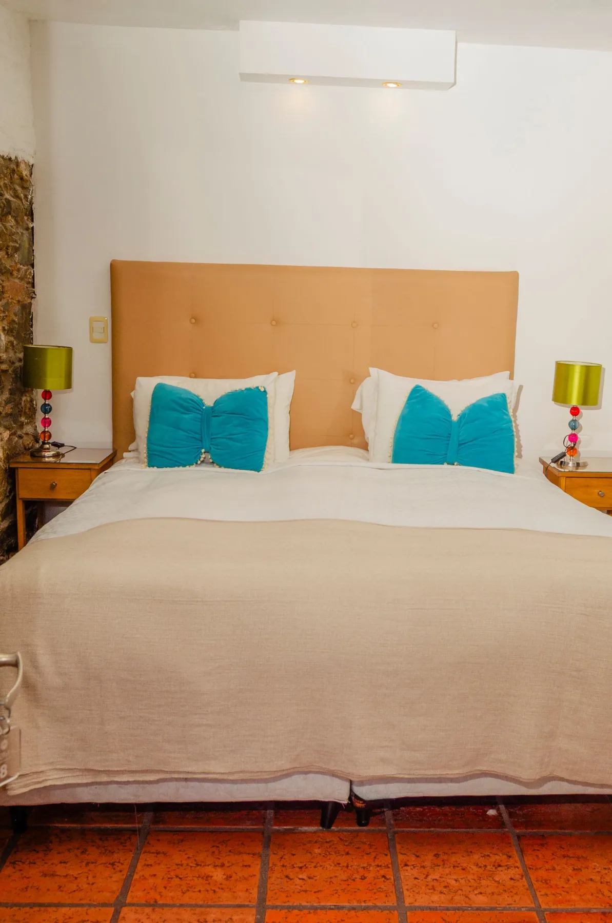 Cama con cojines decorativos de color verde azulado y lámparas de noche.