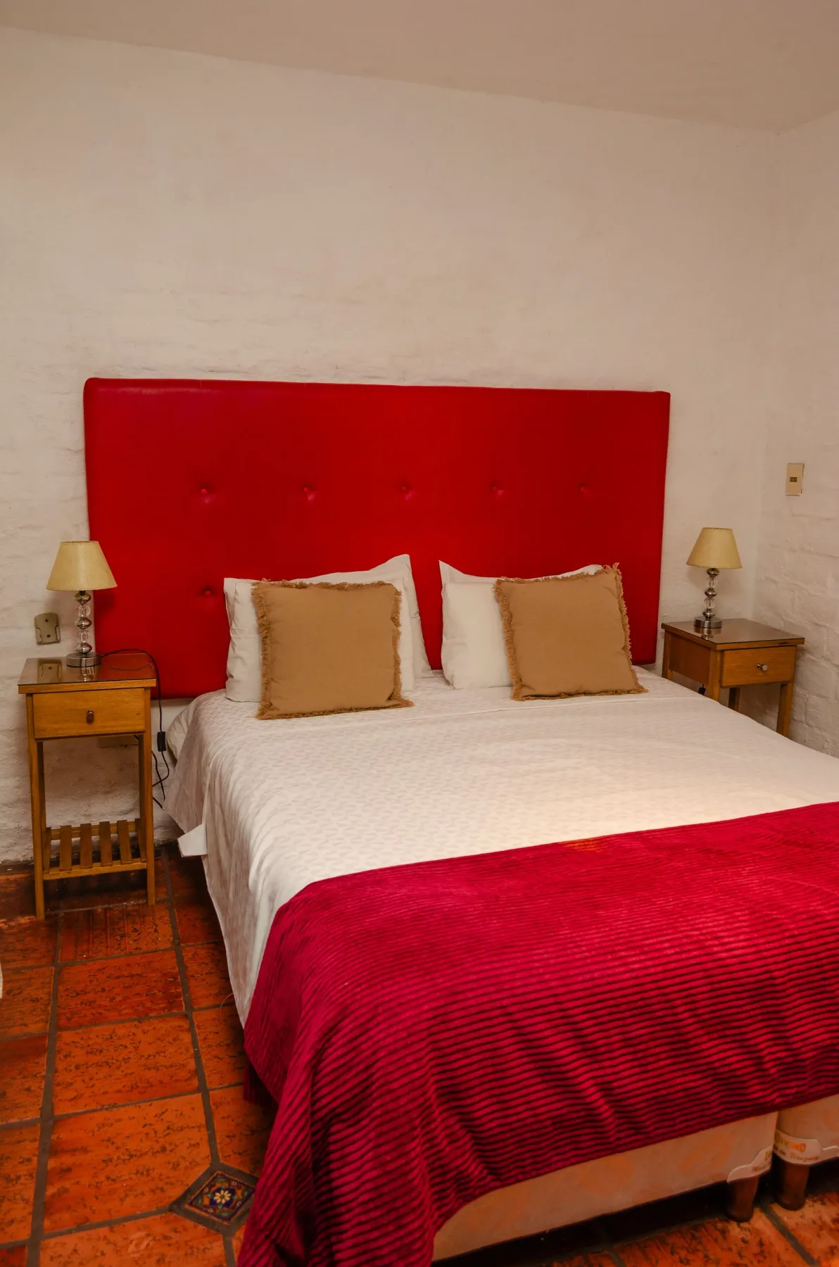 Cama doble con cabecero rojo y suelo de baldosas de terracota.