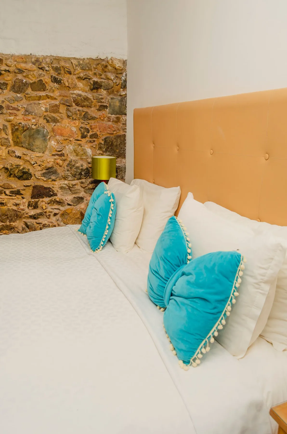 Cama con cojines decorativos azules junto a una pared de piedra vista.