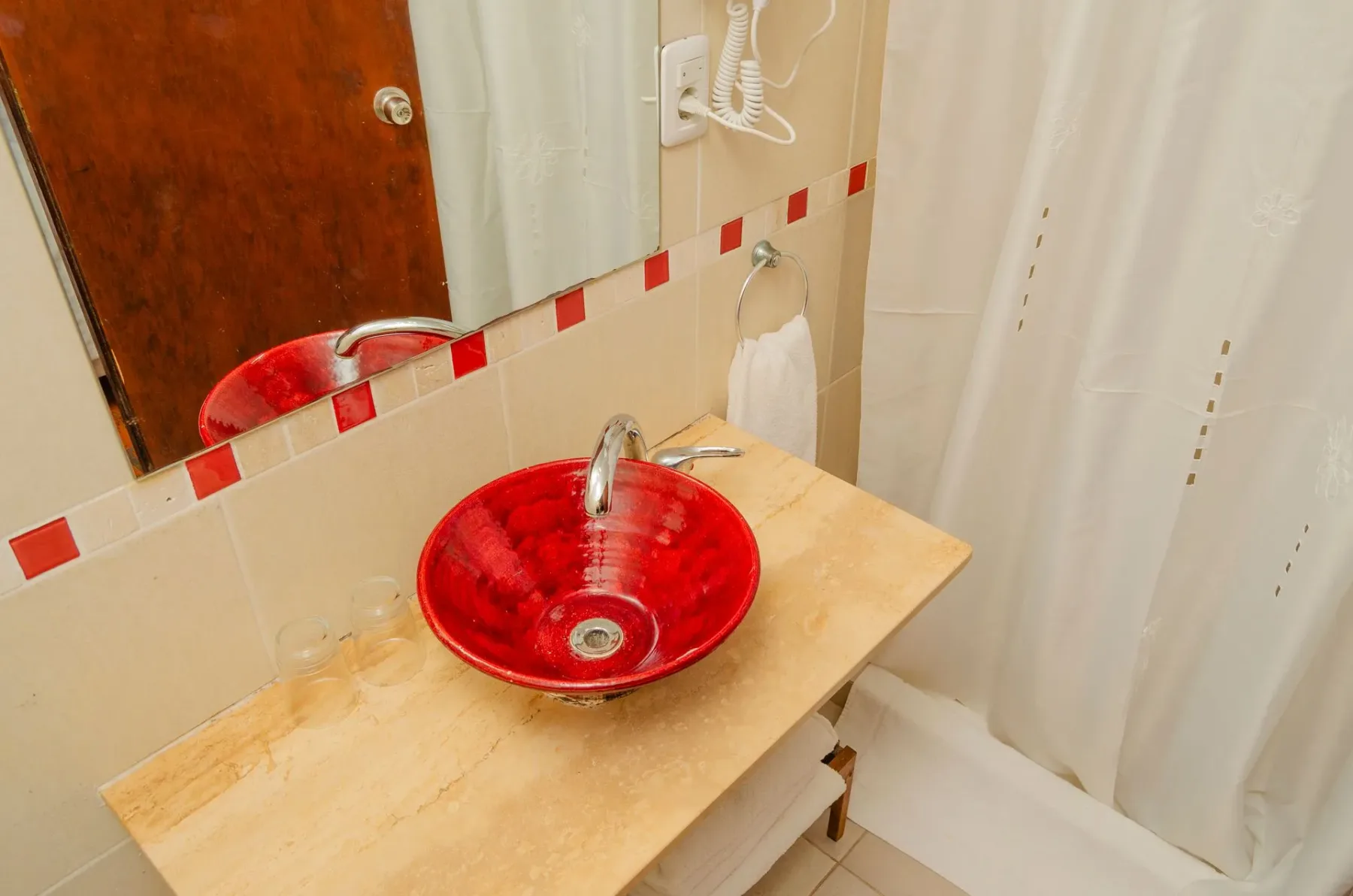 Baño con un lavabo rojo sobre encimera y pared alicatada.