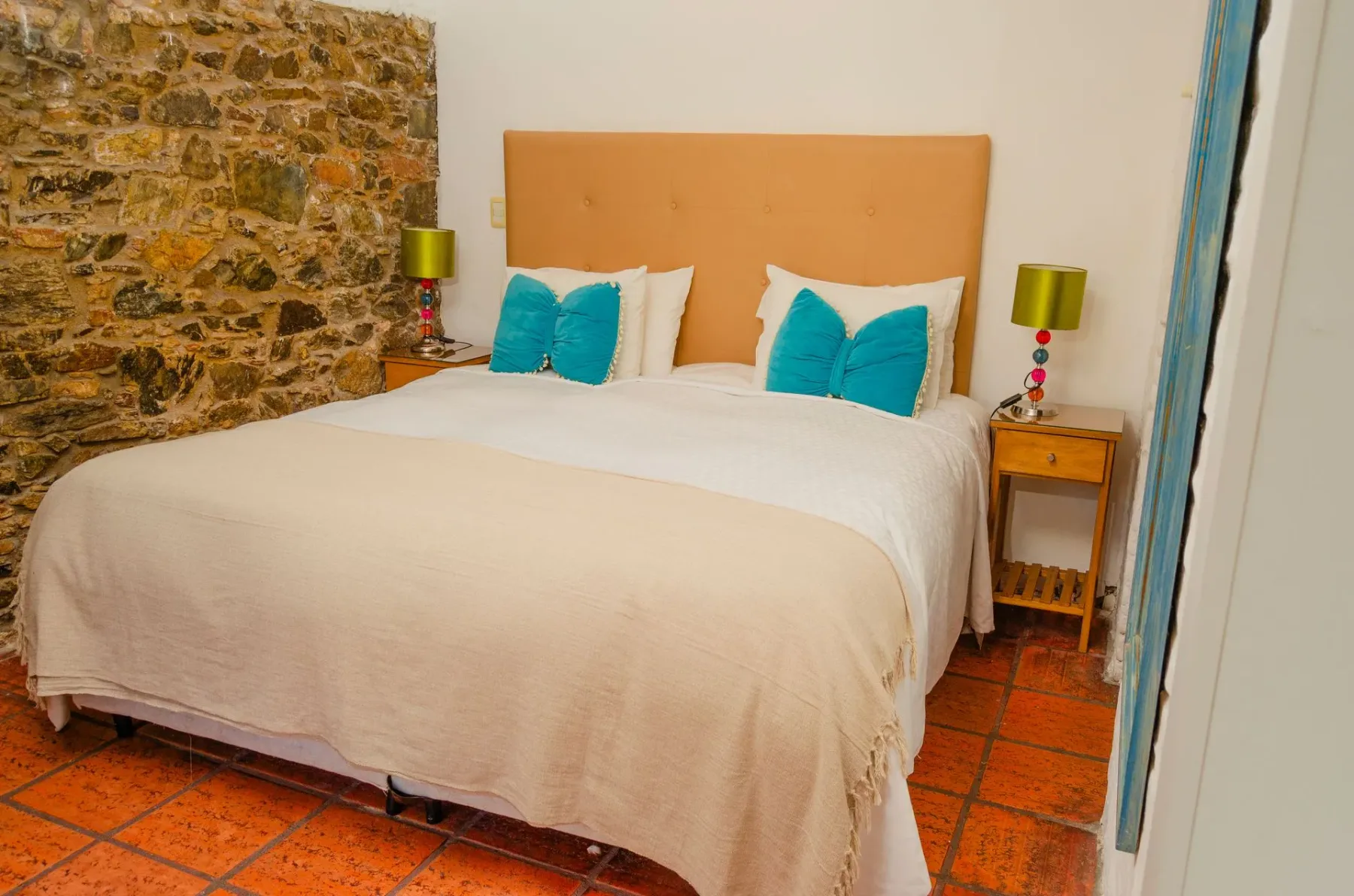 Cama doble con detalles en verde azulado en una habitación con paredes de piedra.