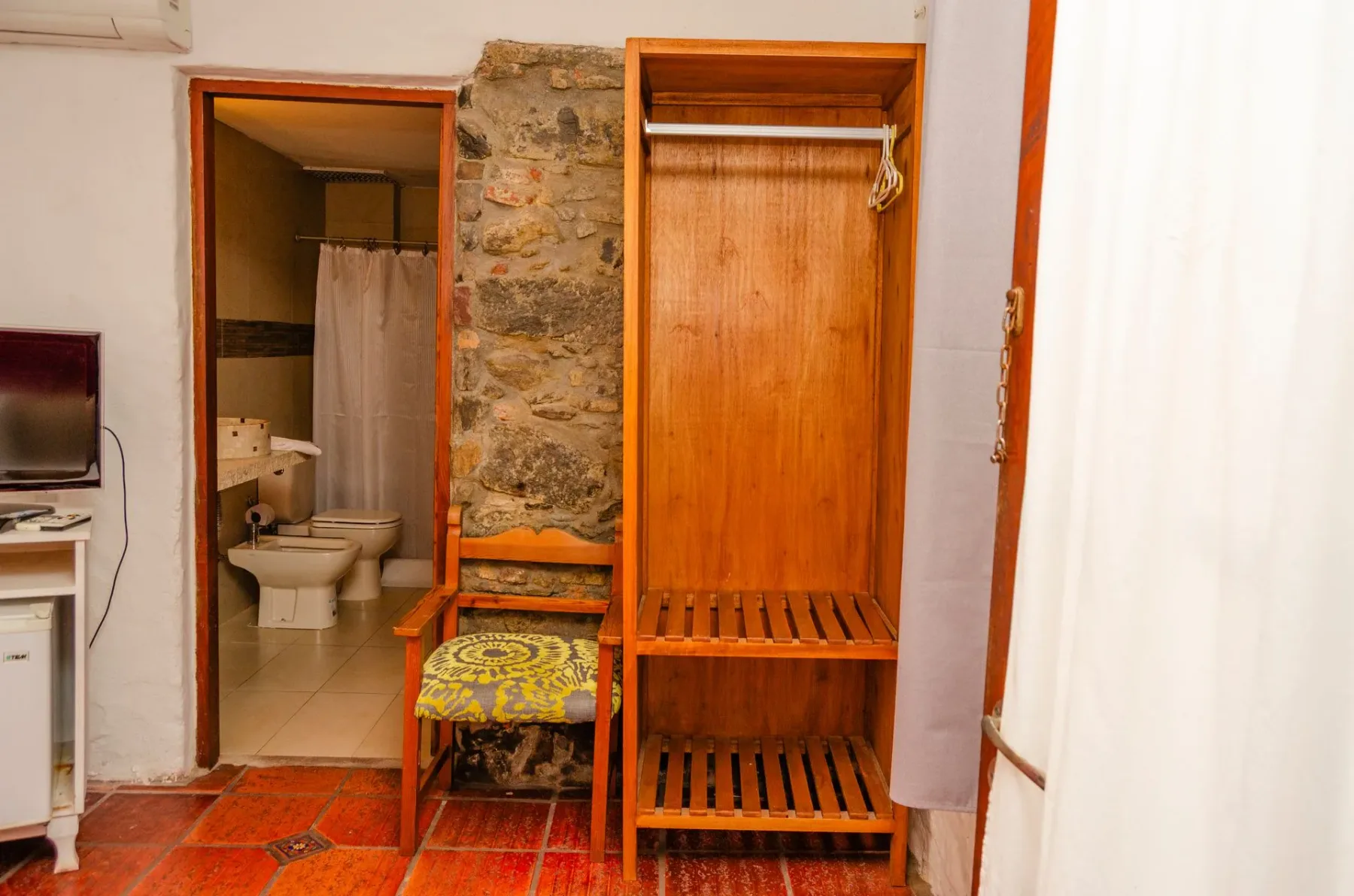 Habitación con un armario de madera abierto y pared de piedra.