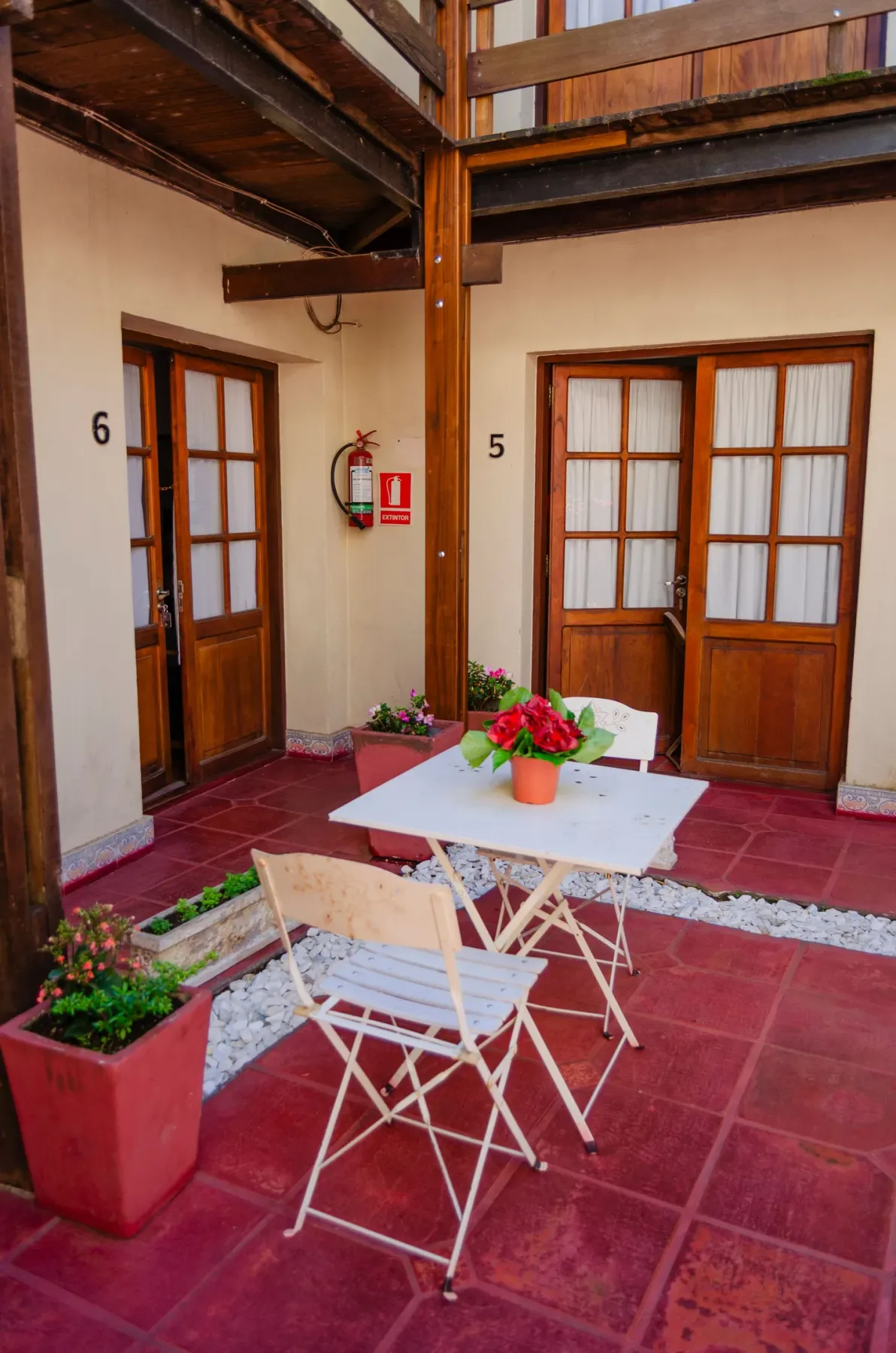 Patio con suelo de baldosas, una mesa con flores y puertas numeradas 5 y 6.