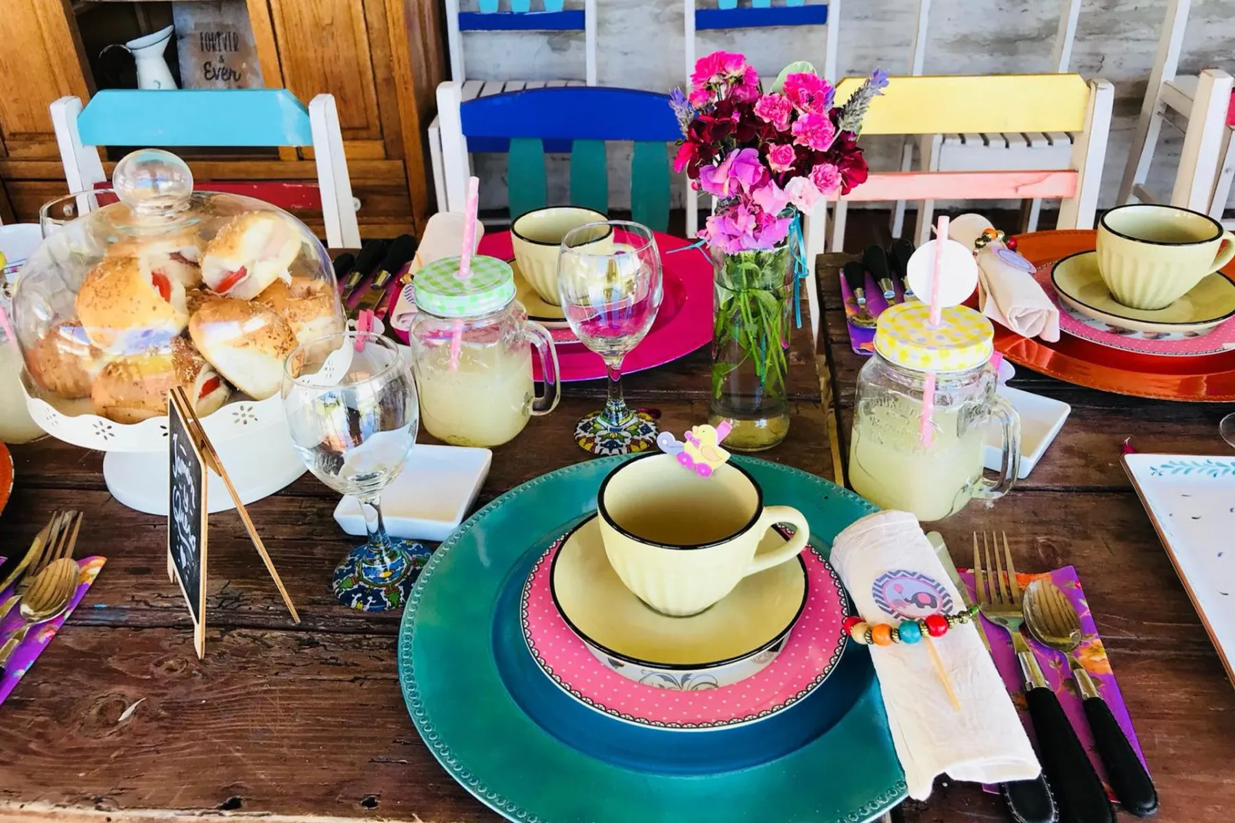 Mesa preparada para el té de la tarde con pasteles, bebidas y flores.