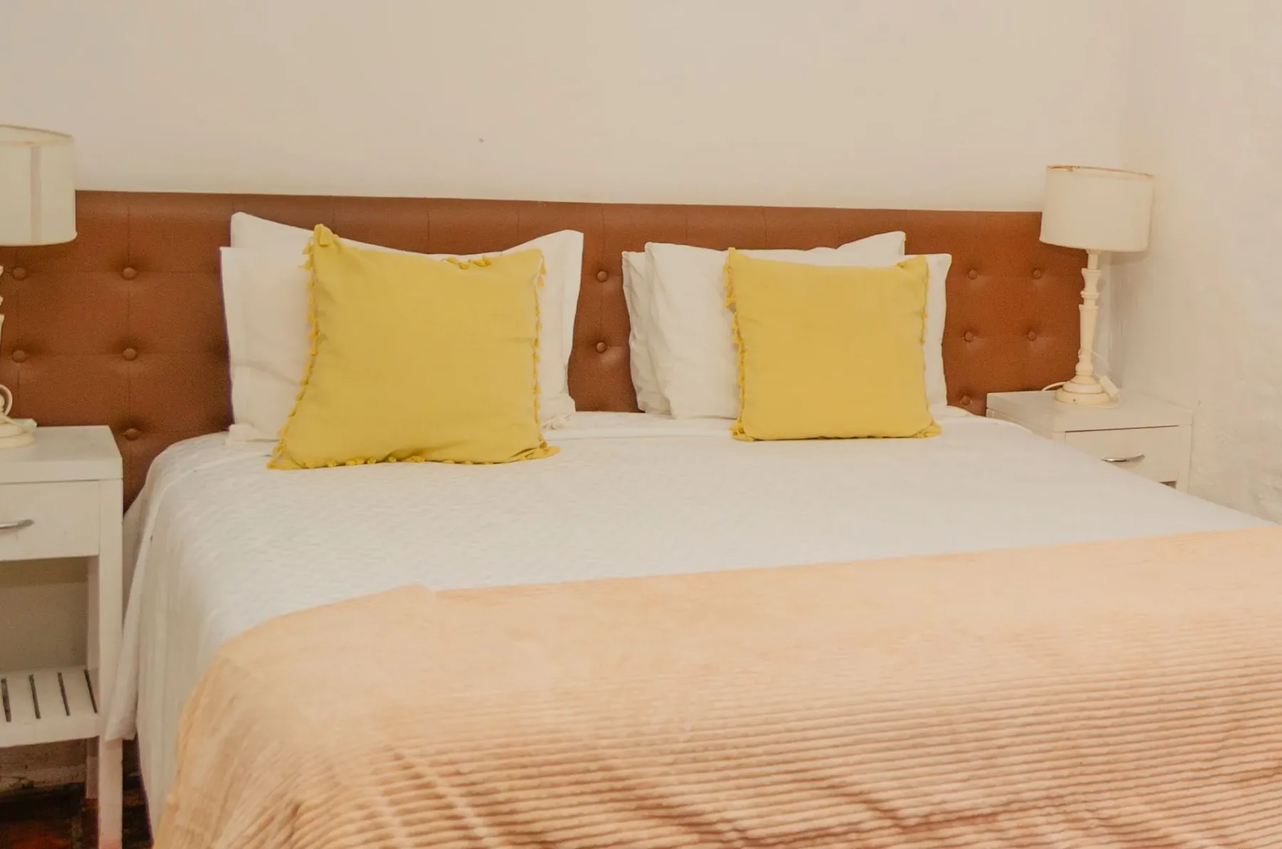 Cama con cabecero tapizado en marrón y cojines decorativos amarillos.
