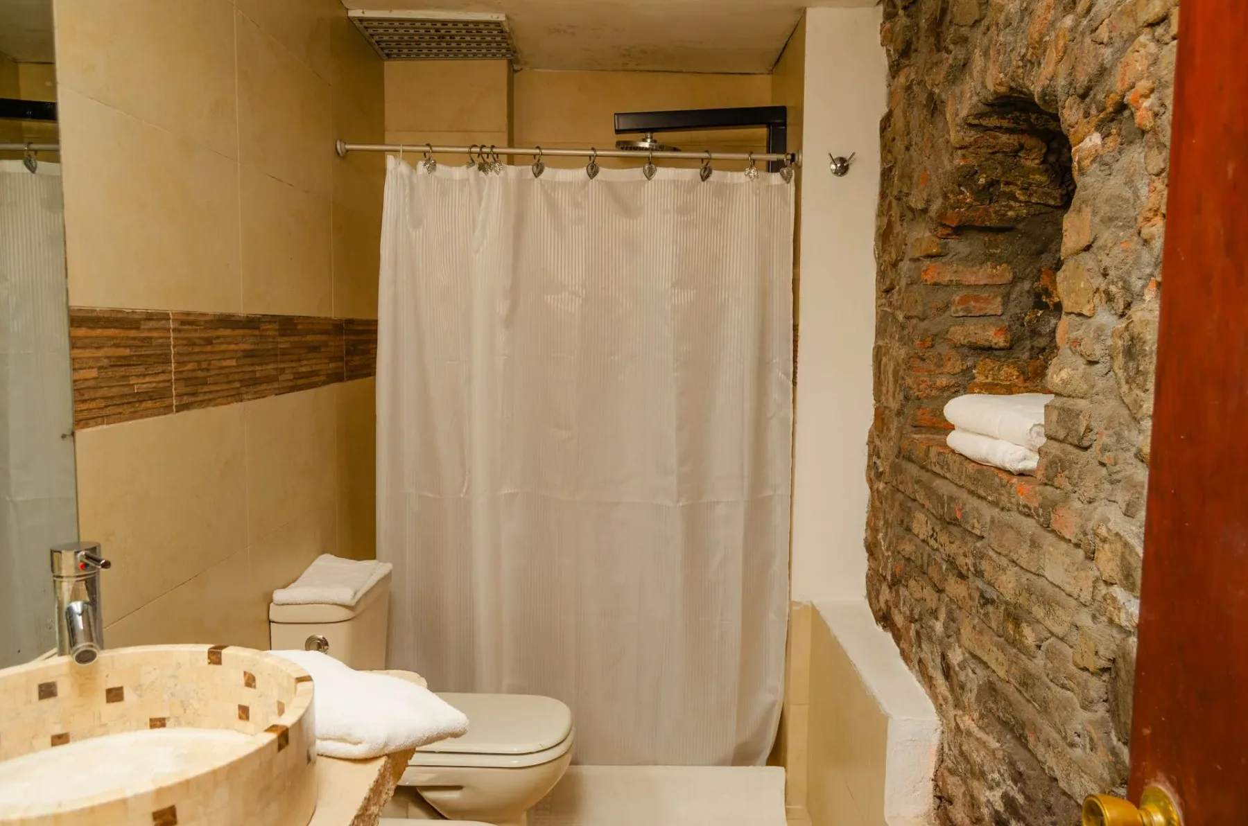 Baño con una pared decorativa de piedra y ducha.