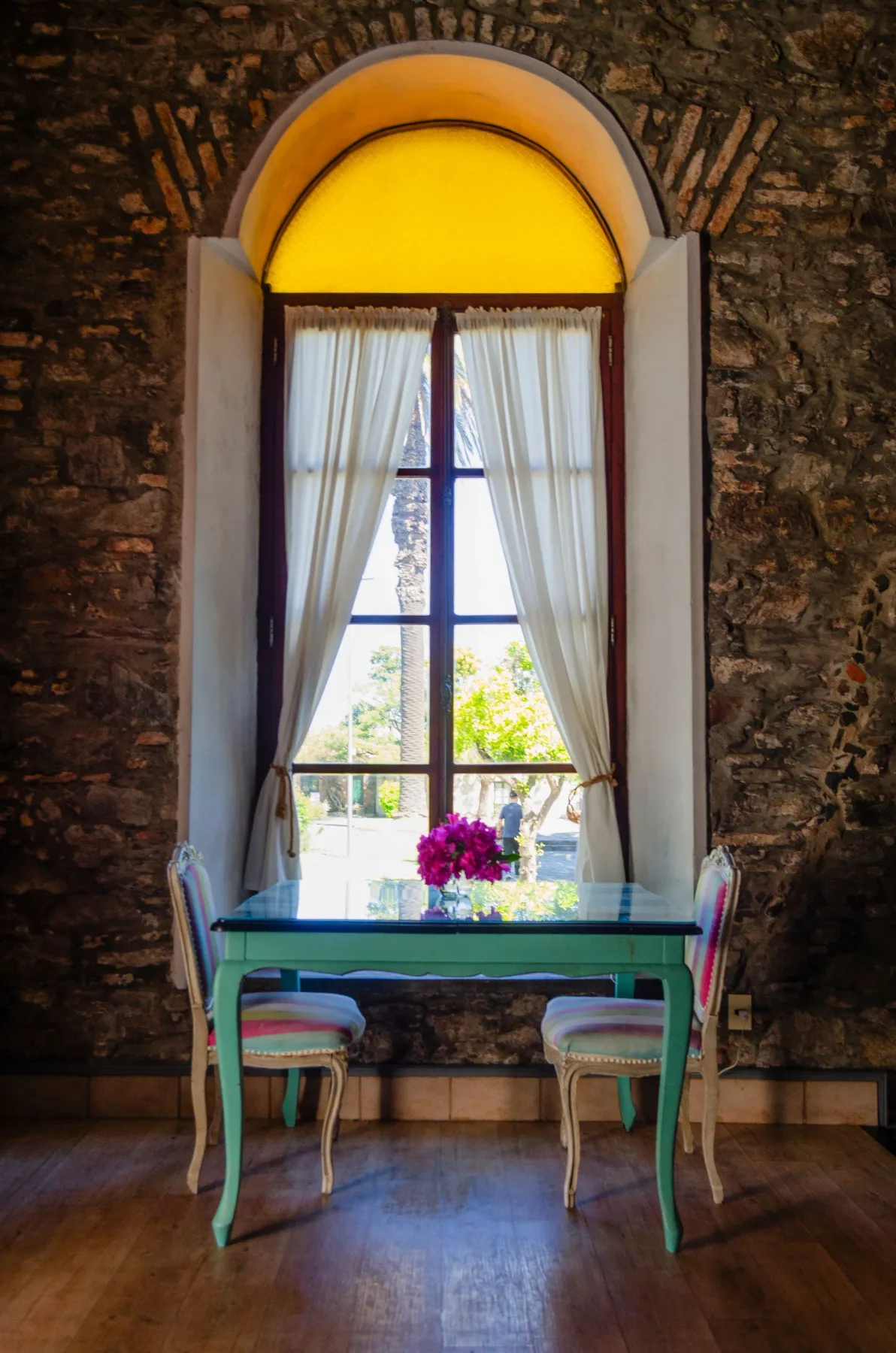 Mesa de comedor pequeña junto a una ventana en arco y una pared de piedra.