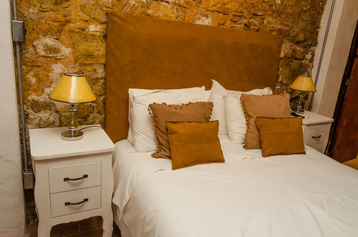 Cama con mesas de noche junto a una pared de piedra rústica.