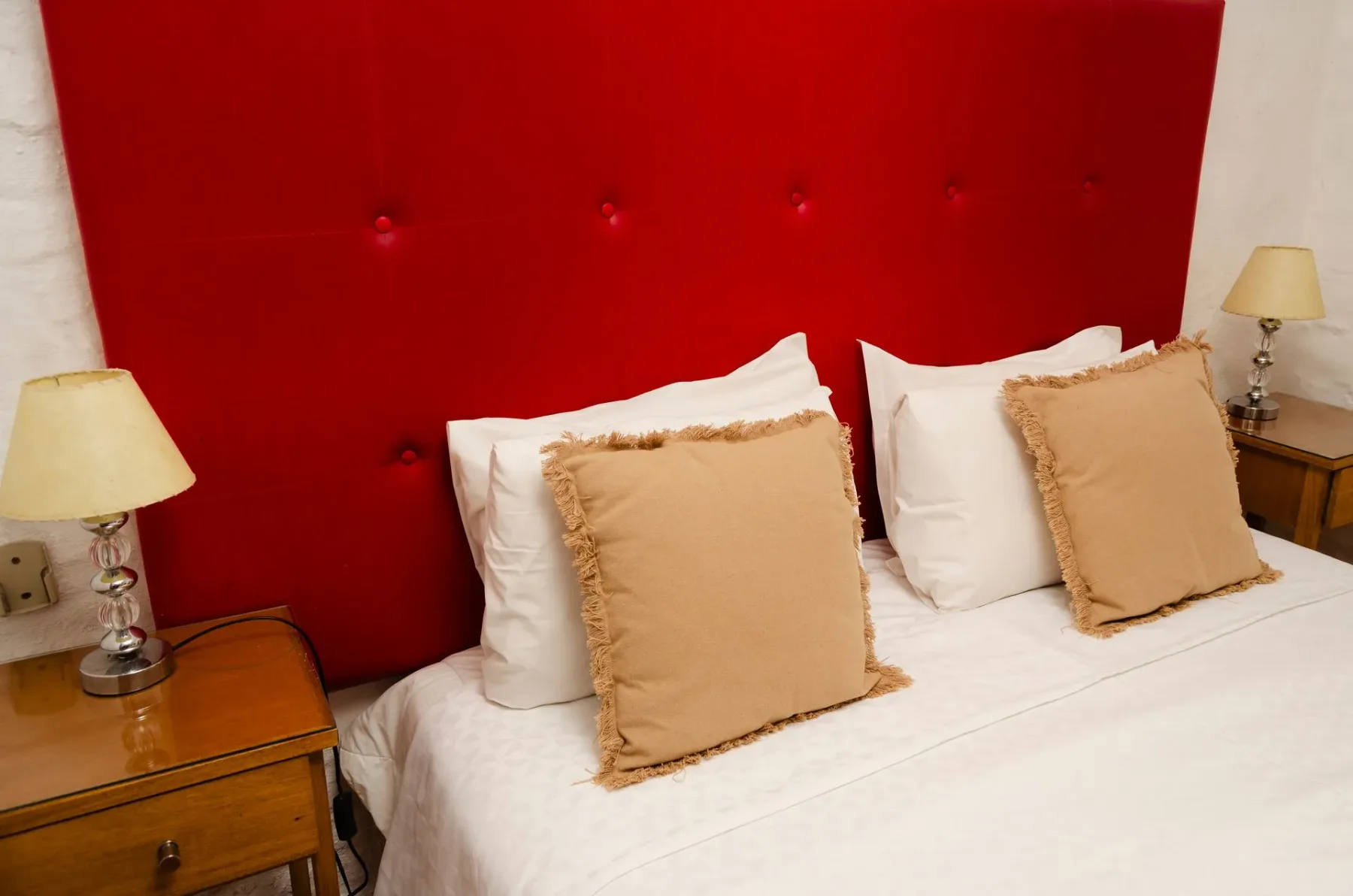 Cama con cabecero tapizado en rojo y lámparas de noche.