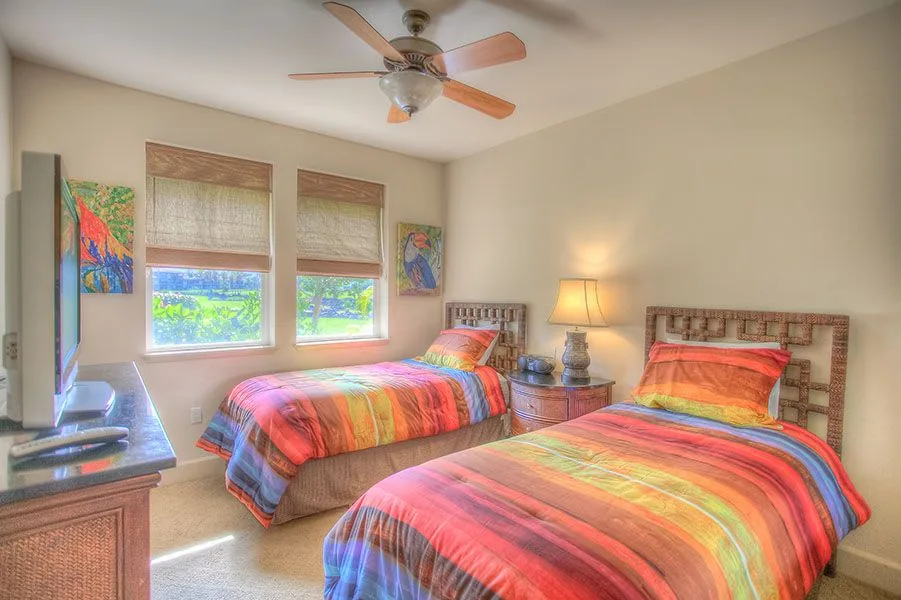 Un dormitorio con dos camas cubiertas con ropa de cama a rayas de colores y ventanas con persianas tejidas.