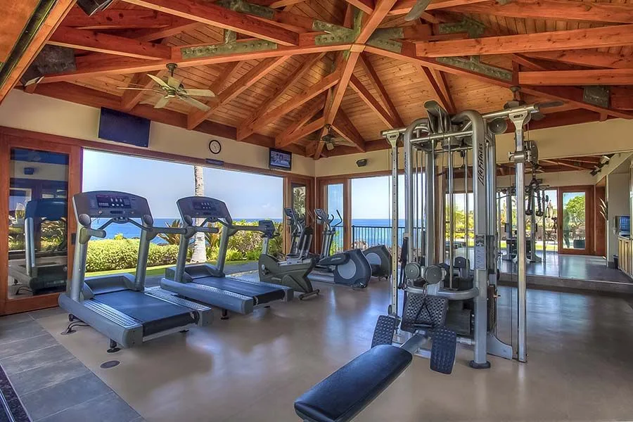 Un gimnasio con cintas de correr y equipos de fuerza junto a grandes ventanales.