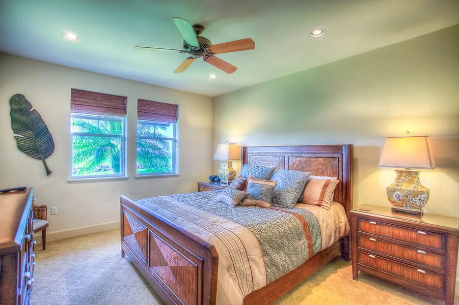 Un dormitorio con cama de madera, ropa de cama estampada y dos ventanas.