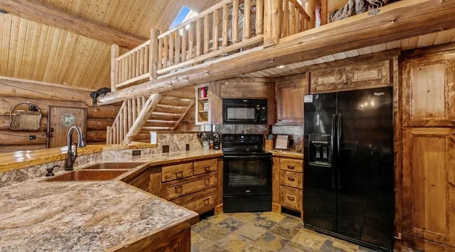 Una cocina rústica con gabinetes de madera, encimeras de piedra y un refrigerador negro.