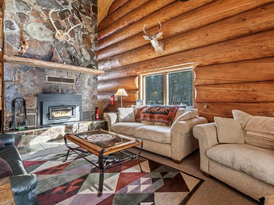 A log-cabin living room with seating around a fireplace and coffee table.
