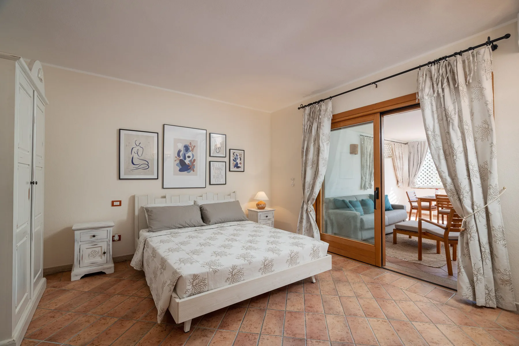 A bedroom with a bed beneath framed artwork and a curtained glass door.