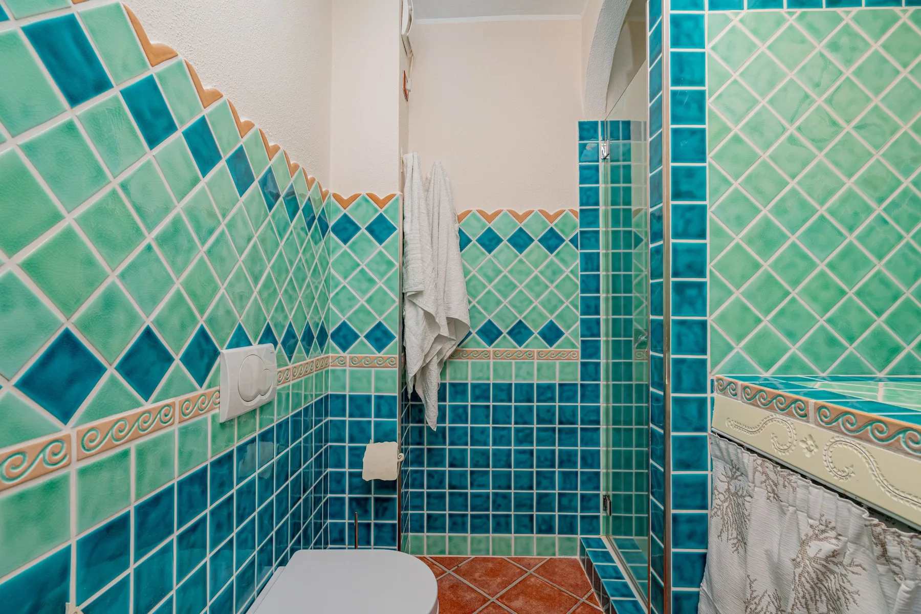 A tiled bathroom with a shower area and a white towel hanging on the wall.