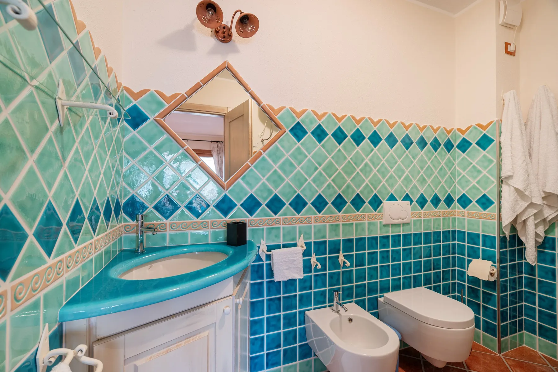 A tiled bathroom with a sink, bidet, toilet, and wall mirror.