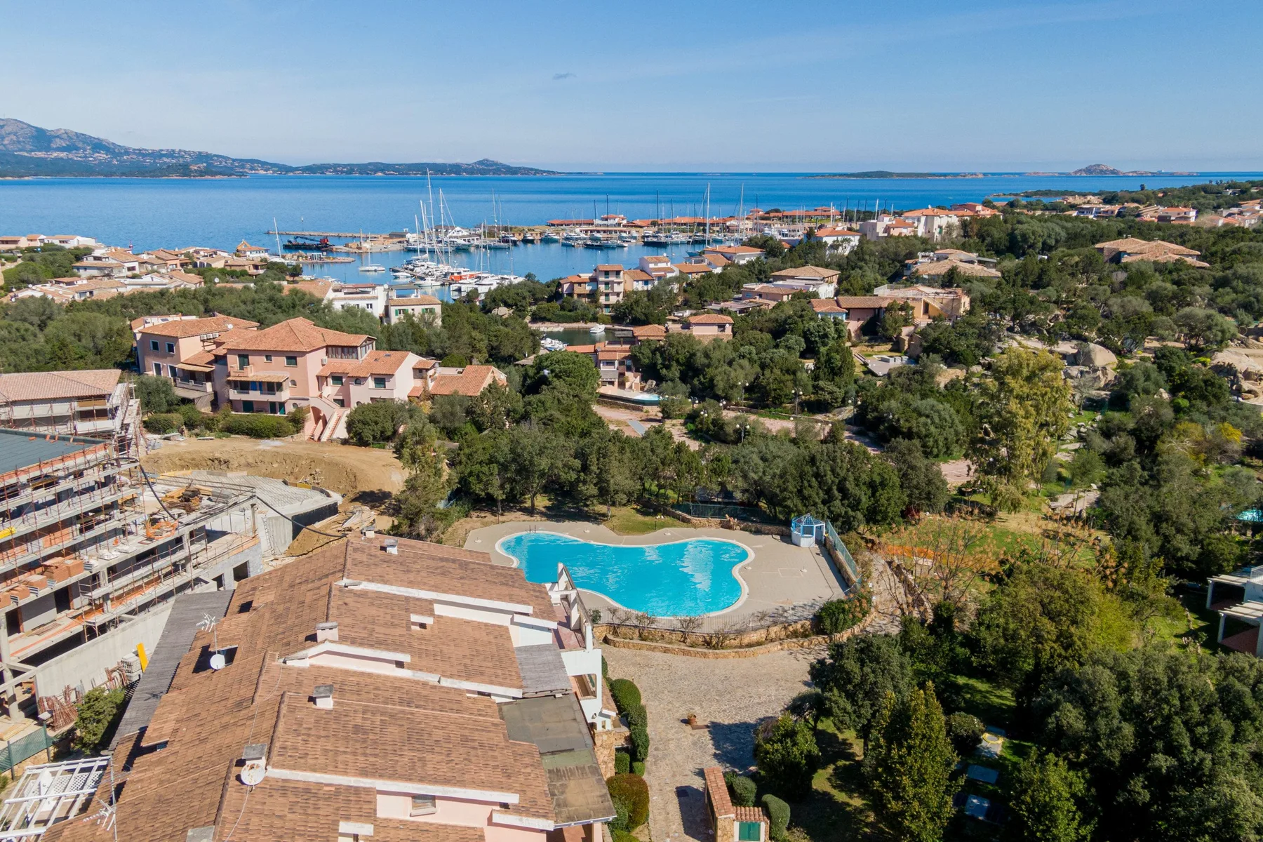 A coastal residential area overlooks a marina, with a swimming pool in the foreground.