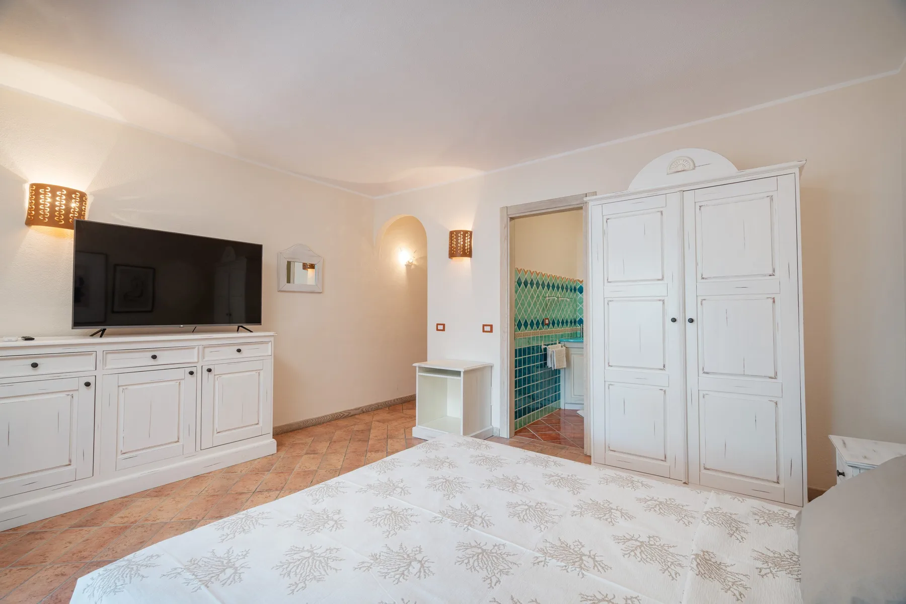 A bedroom with a large bed, white wardrobe, and television.