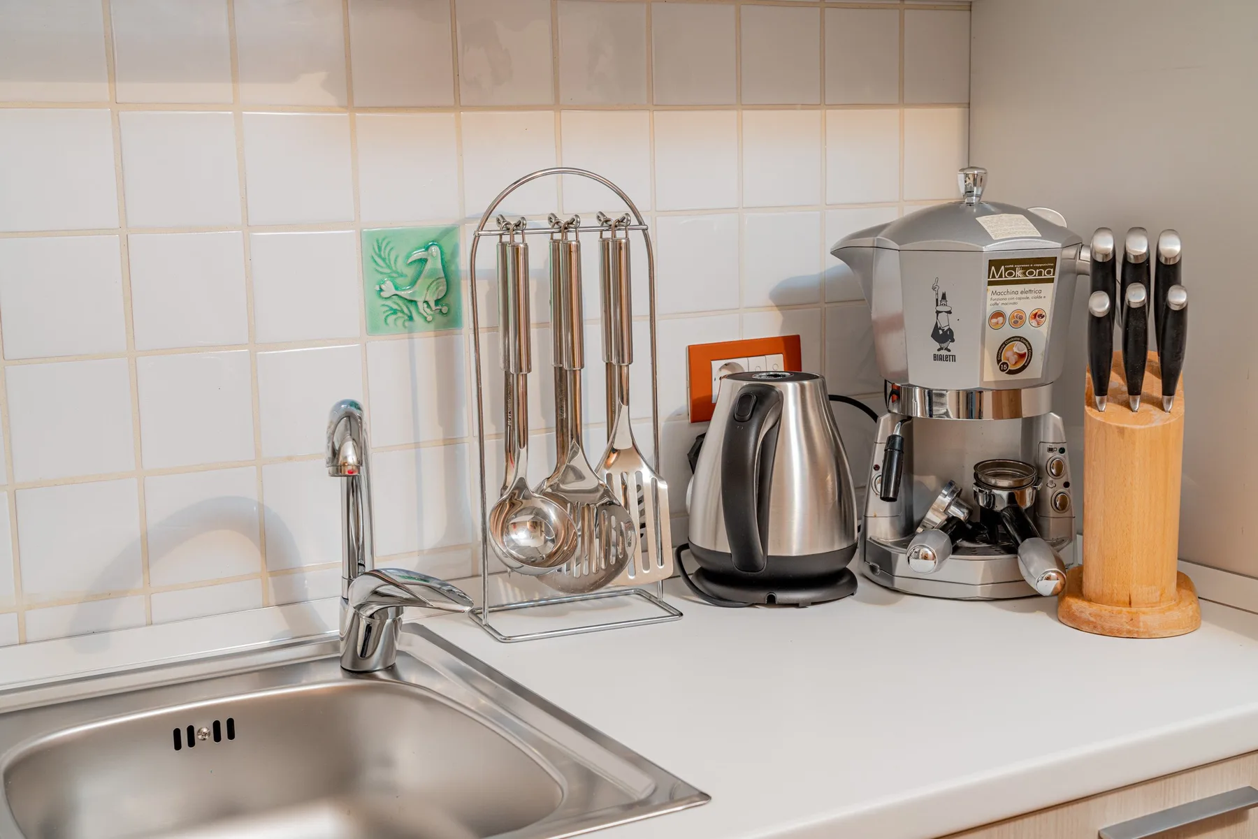 A kitchen counter with a sink, kettle, and coffee machine.