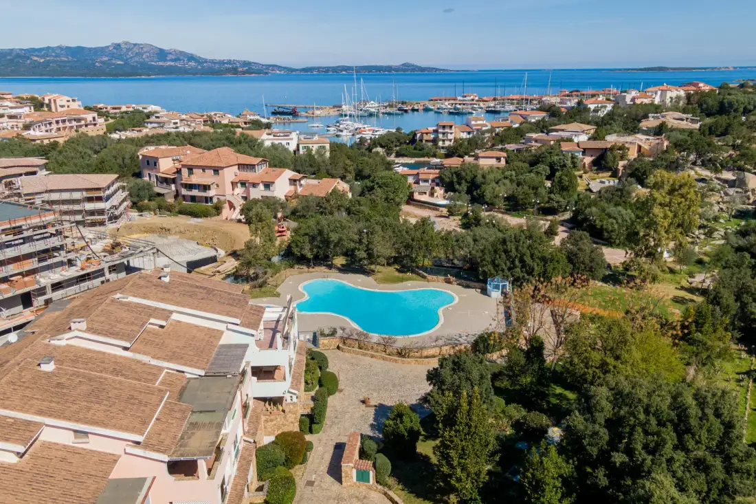 Aerial view of a coastal resort with a swimming pool, buildings, and a marina.