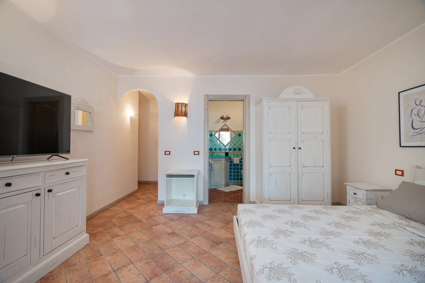 A bedroom with a bed, white cabinets, and a tiled floor.