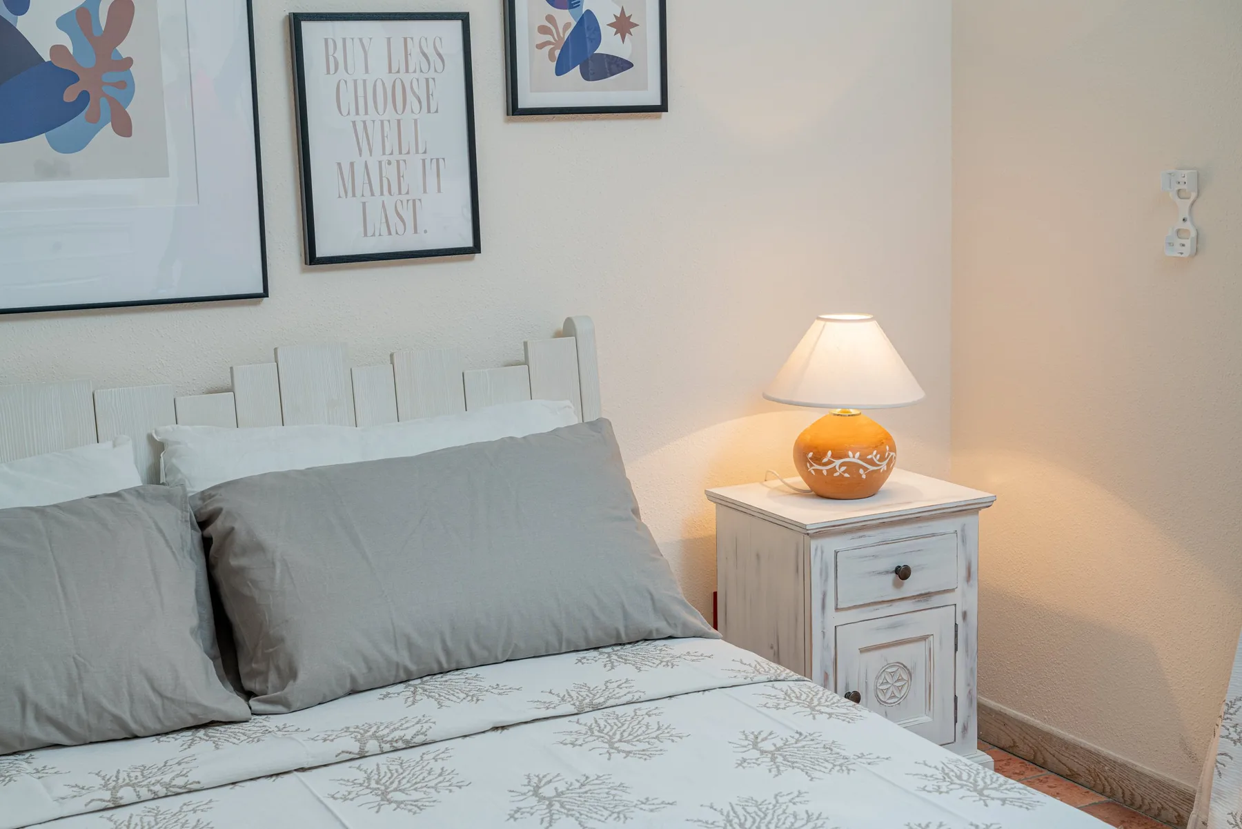 A bedroom features a bed with pale bedding and a lit bedside lamp.