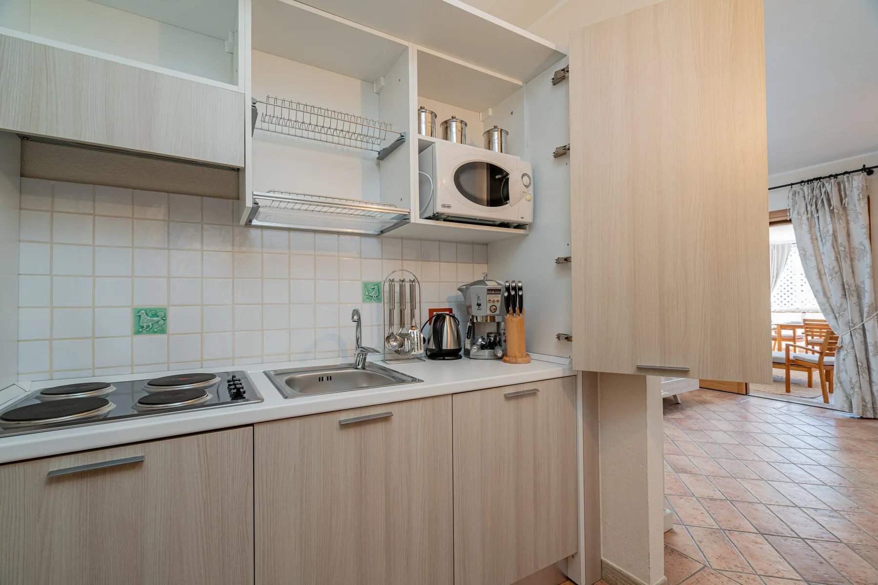 A compact kitchen with a sink, cooktop, and open shelving.