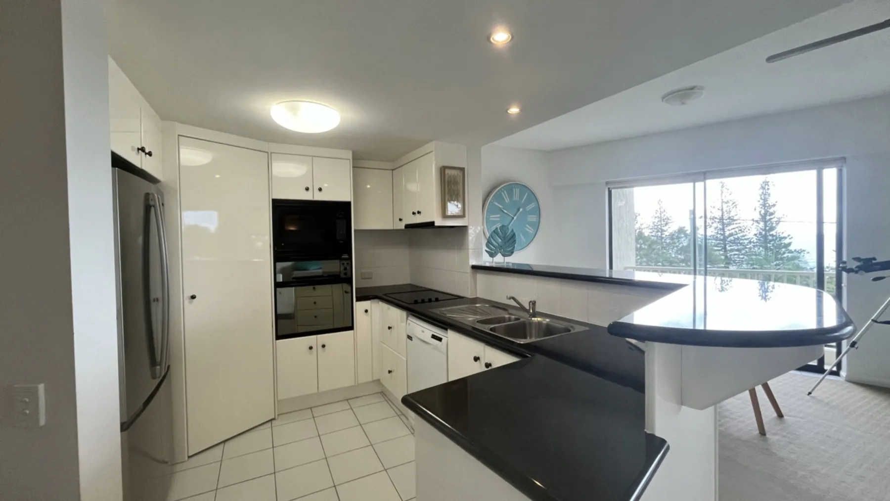 A modern kitchen with dark countertops and a dining area beside the window.