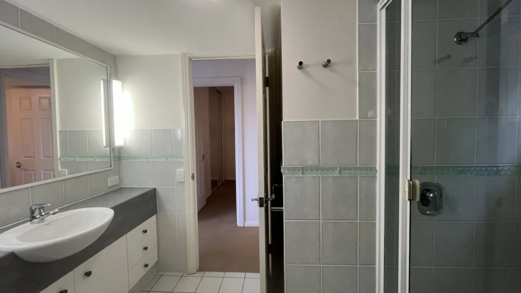 A tiled bathroom with a sink and glass shower is visible.