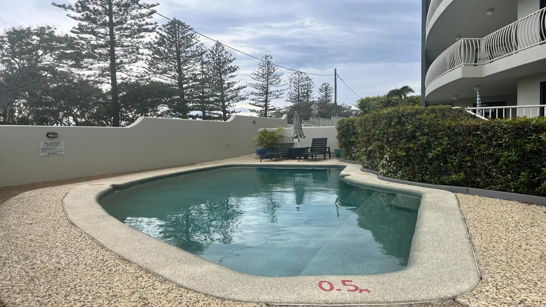 An outdoor swimming pool beside a curved apartment building and landscaped grounds.