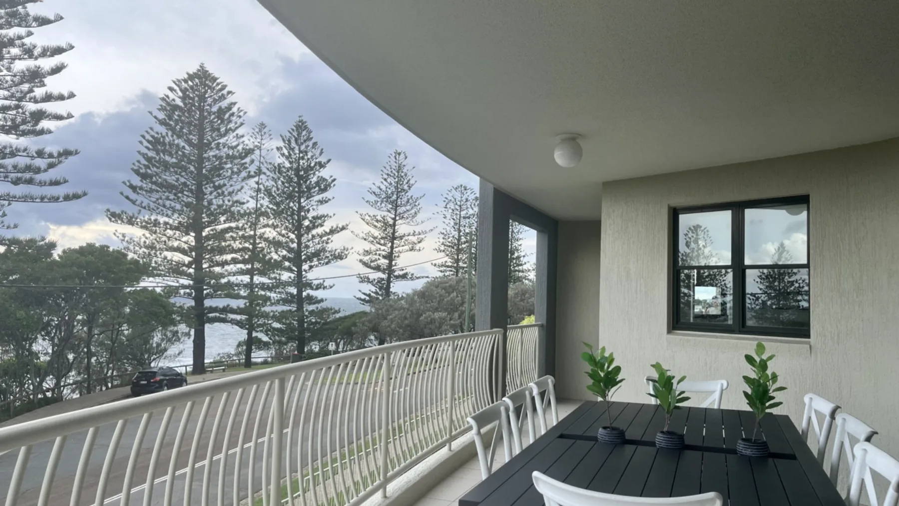 A covered balcony with a dark dining table overlooks trees and water.