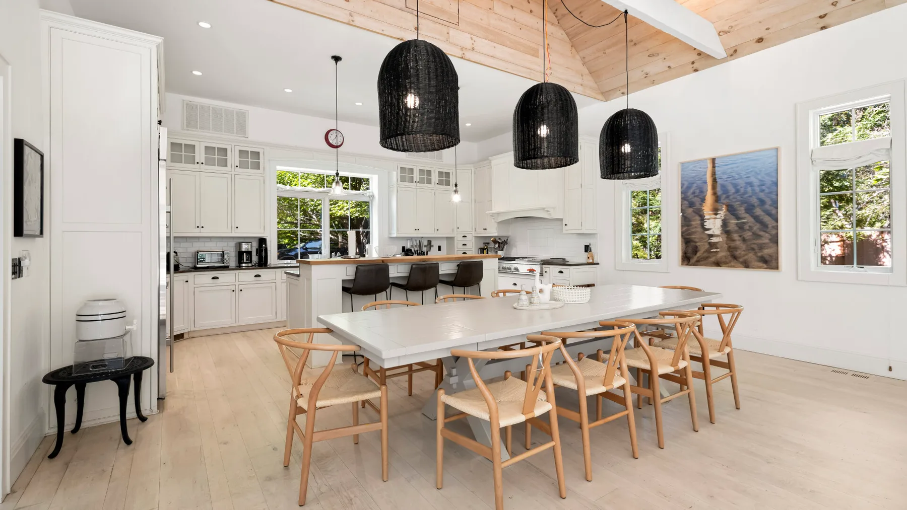 Un comedor luminoso con una mesa larga, sillas de madera y lámparas colgantes.