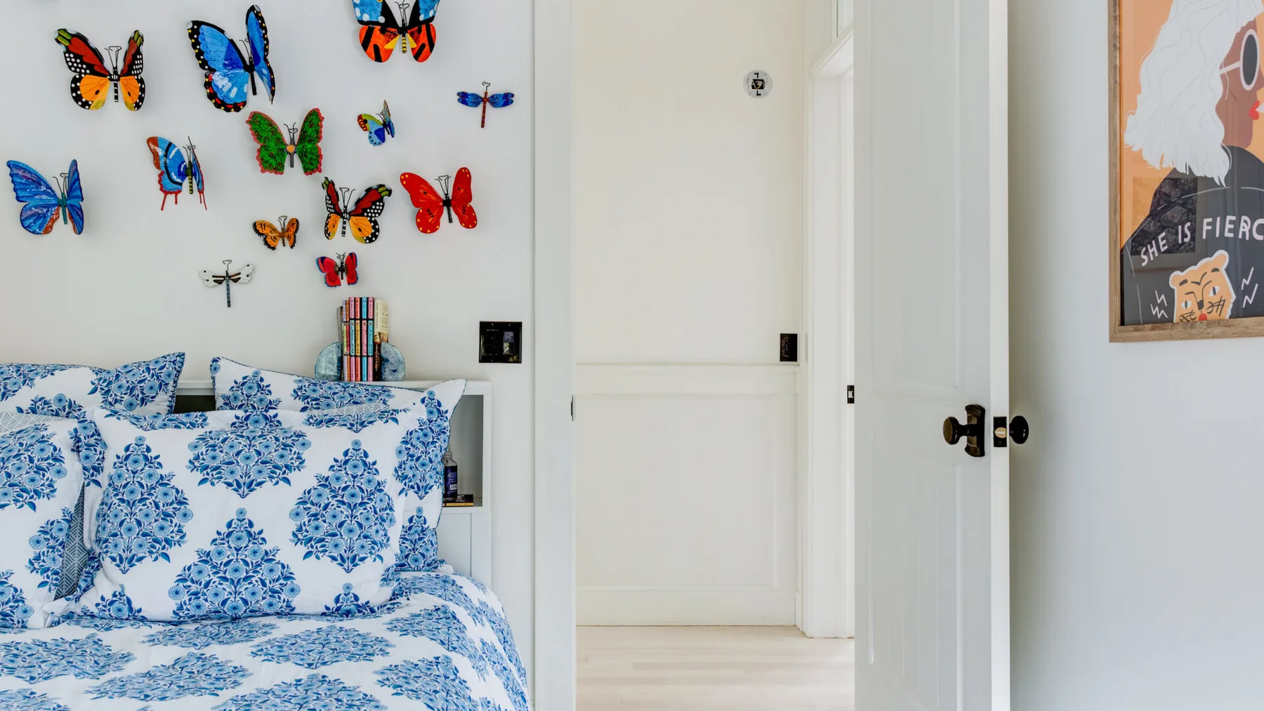 Un dormitorio con ropa de cama estampada en azul y blanco y mariposas de colores en la pared.