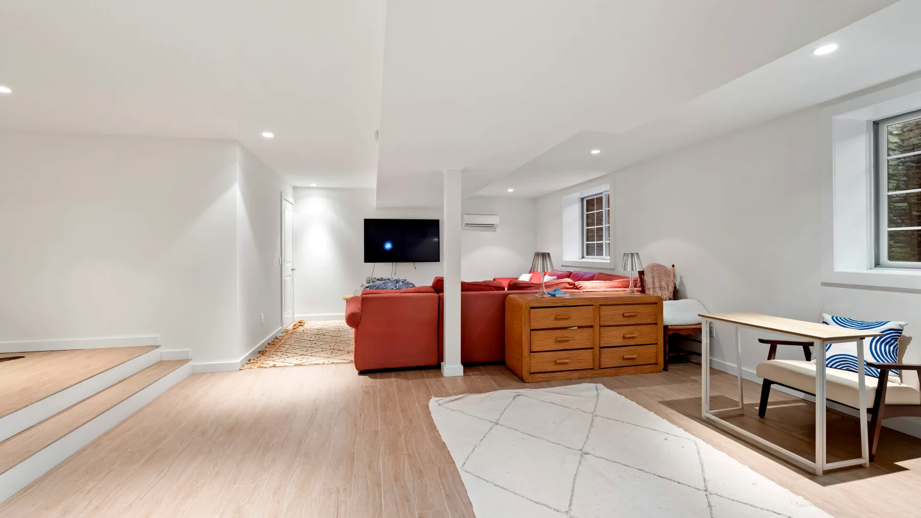 Una luminosa sala en el sótano con asientos rojos y una cómoda de madera.