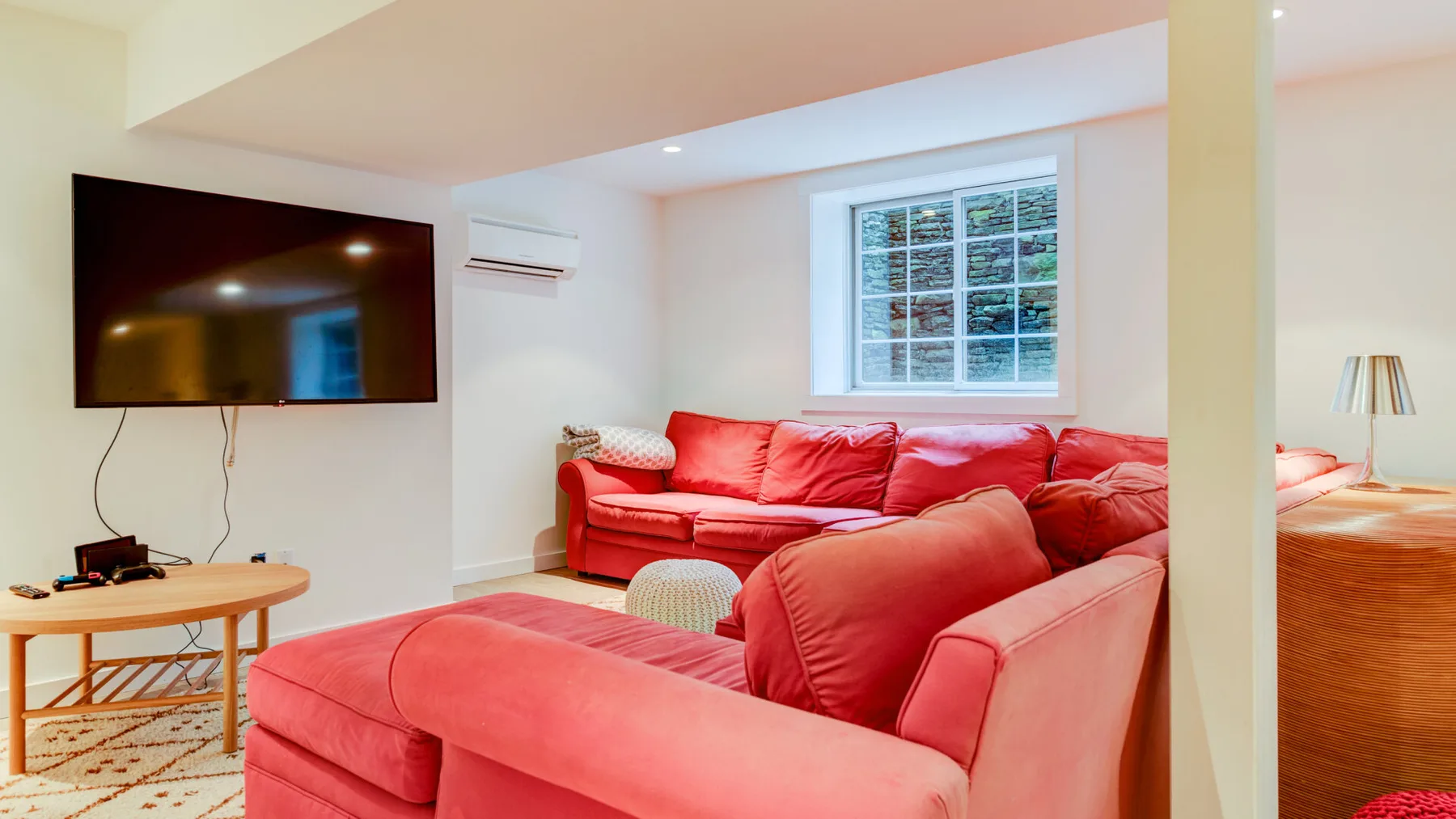 Una sala luminosa con asientos rojos, un televisor montado en la pared y una ventana.