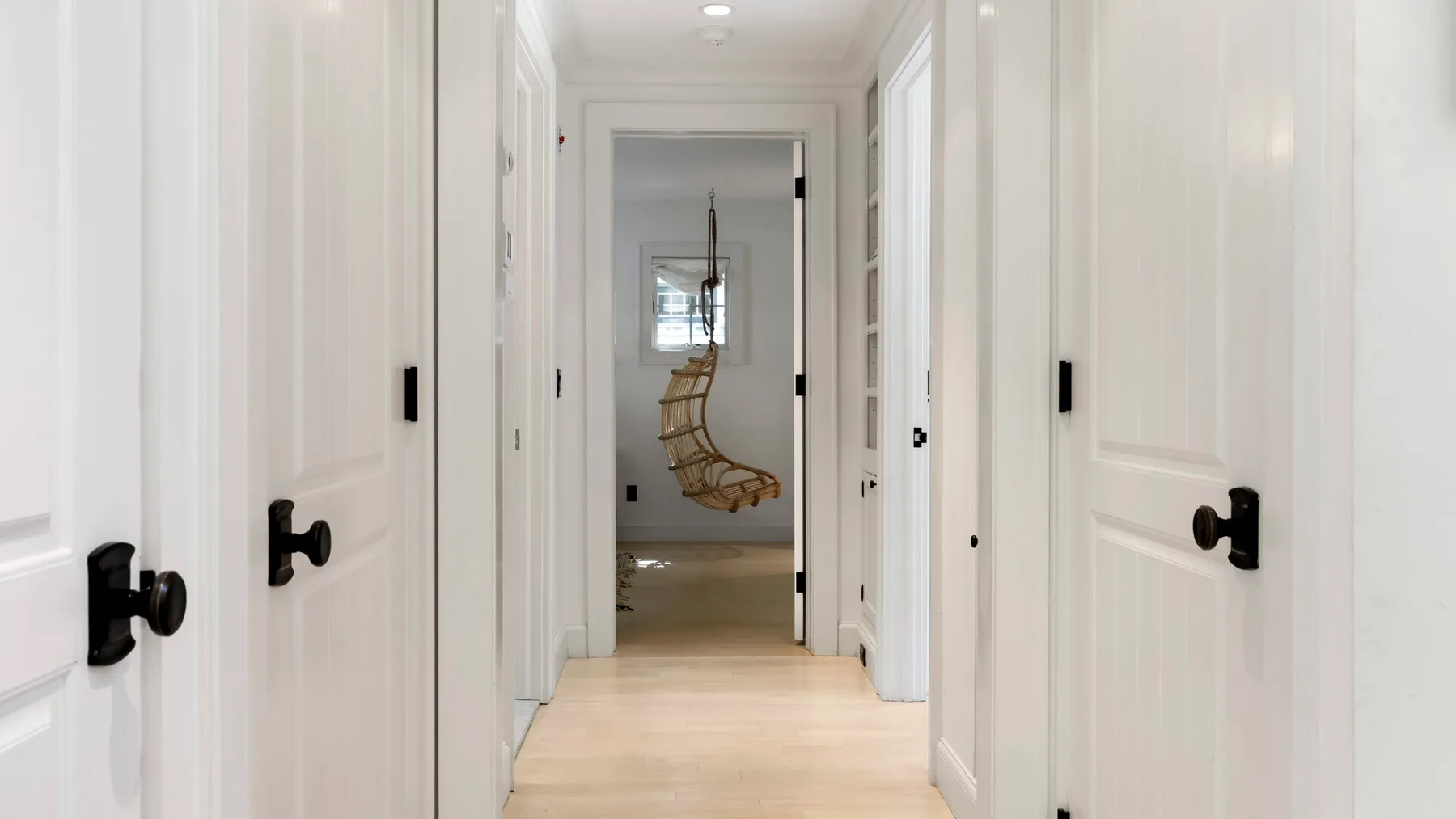 Un pasillo blanco y luminoso conduce a una habitación con una silla colgante.