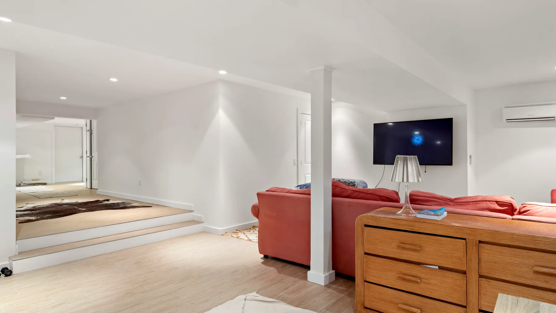 Una sala luminosa con asientos rojos, un televisor y una cómoda de madera.