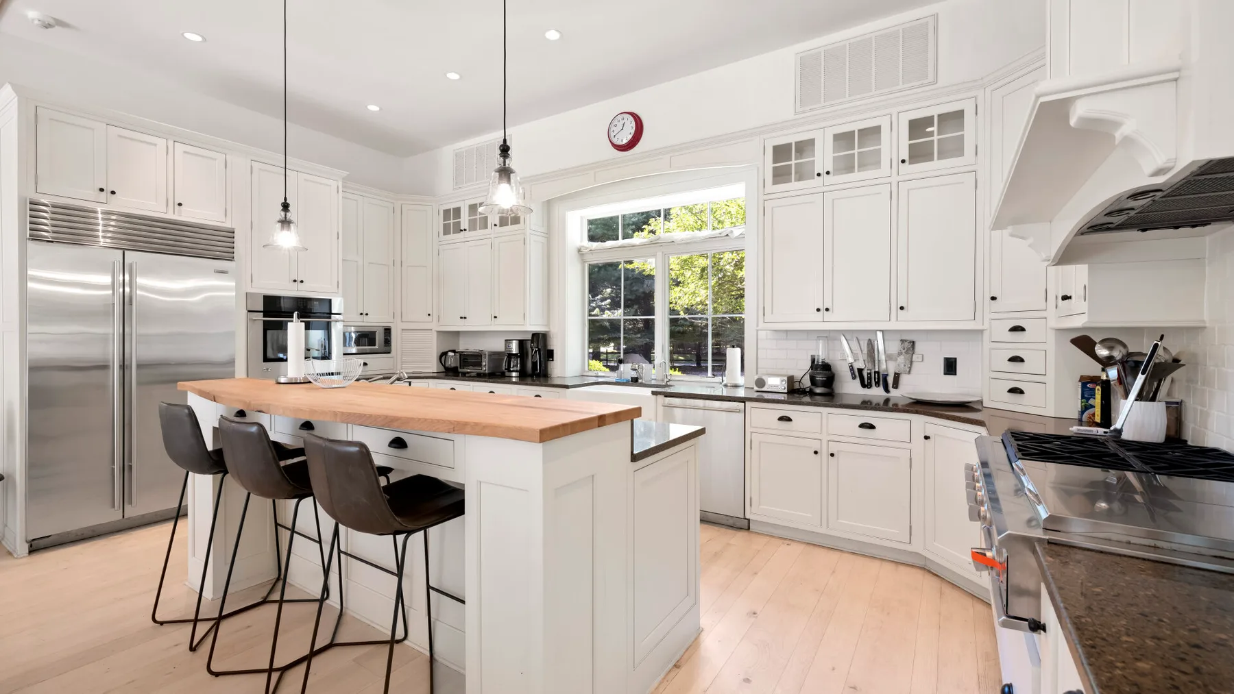 Una cocina blanca y luminosa con una isla grande, electrodomésticos de acero inoxidable y ventanas.
