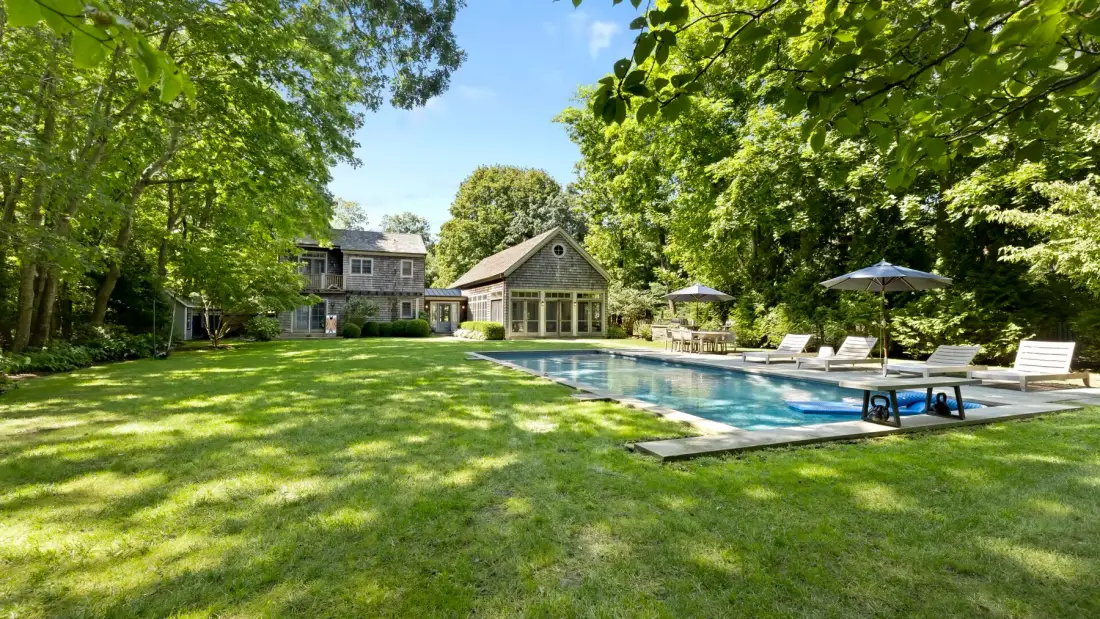 Un patio ajardinado con piscina y asientos para descansar.