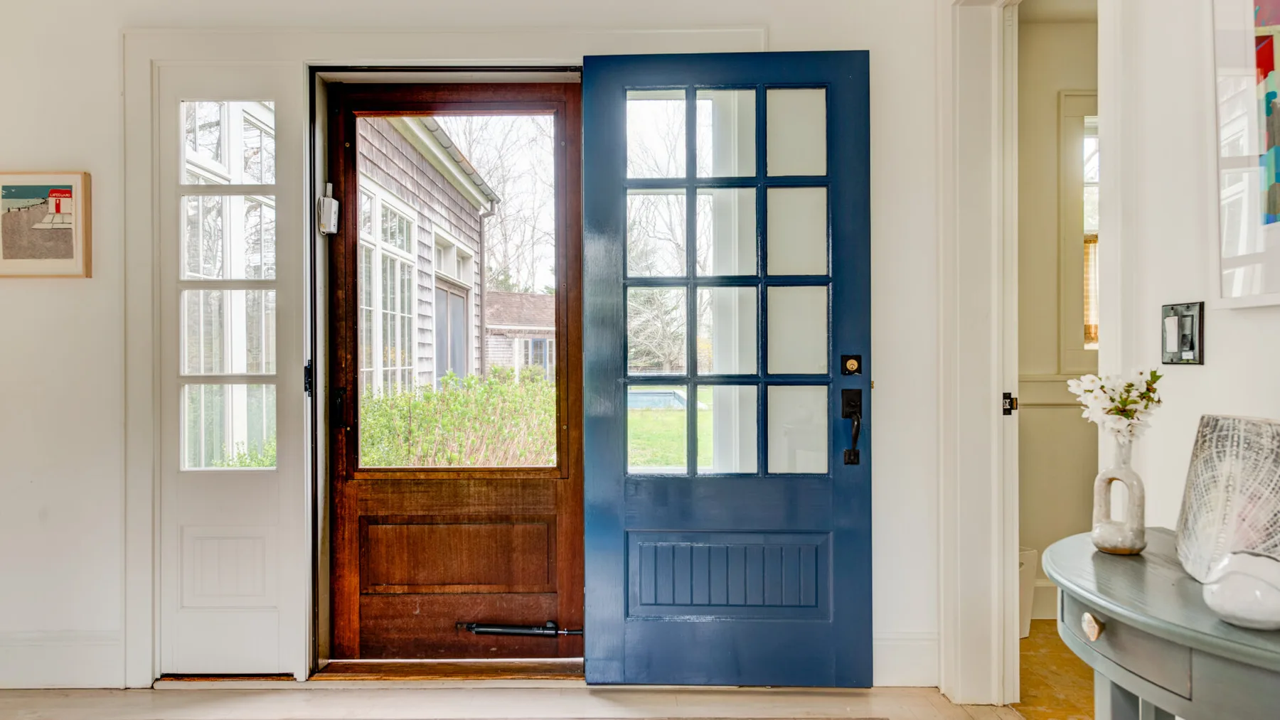 Una entrada con la puerta azul abierta y vistas al jardín.