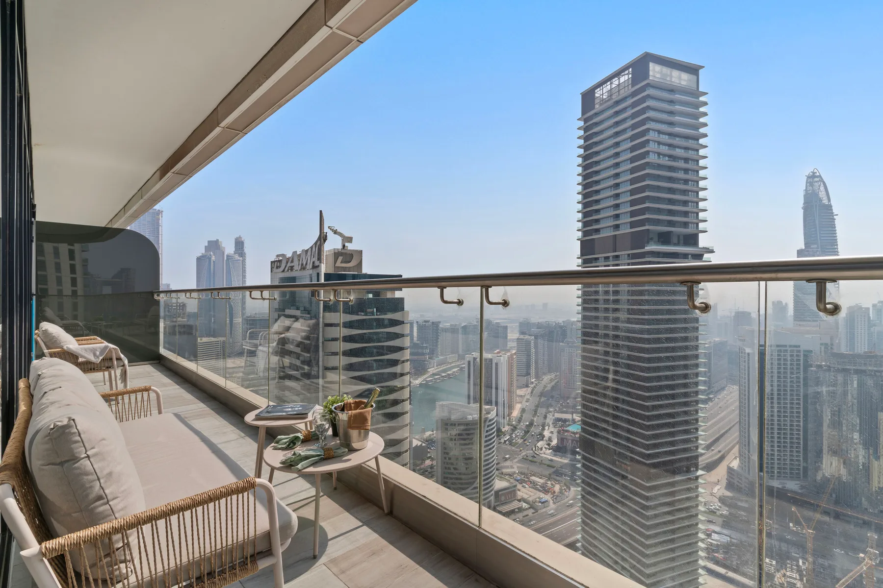 A balcony seating area overlooks a city skyline through a glass railing.