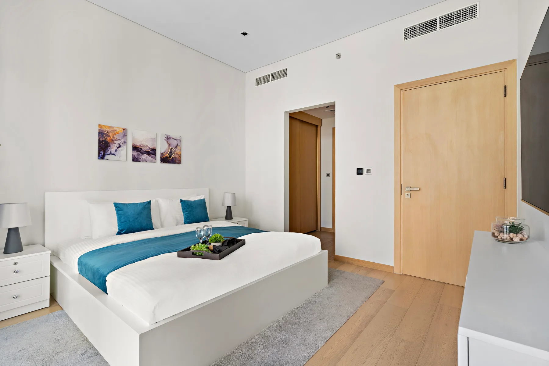 A bright bedroom with a white bed, blue bedding, and artwork above the headboard.