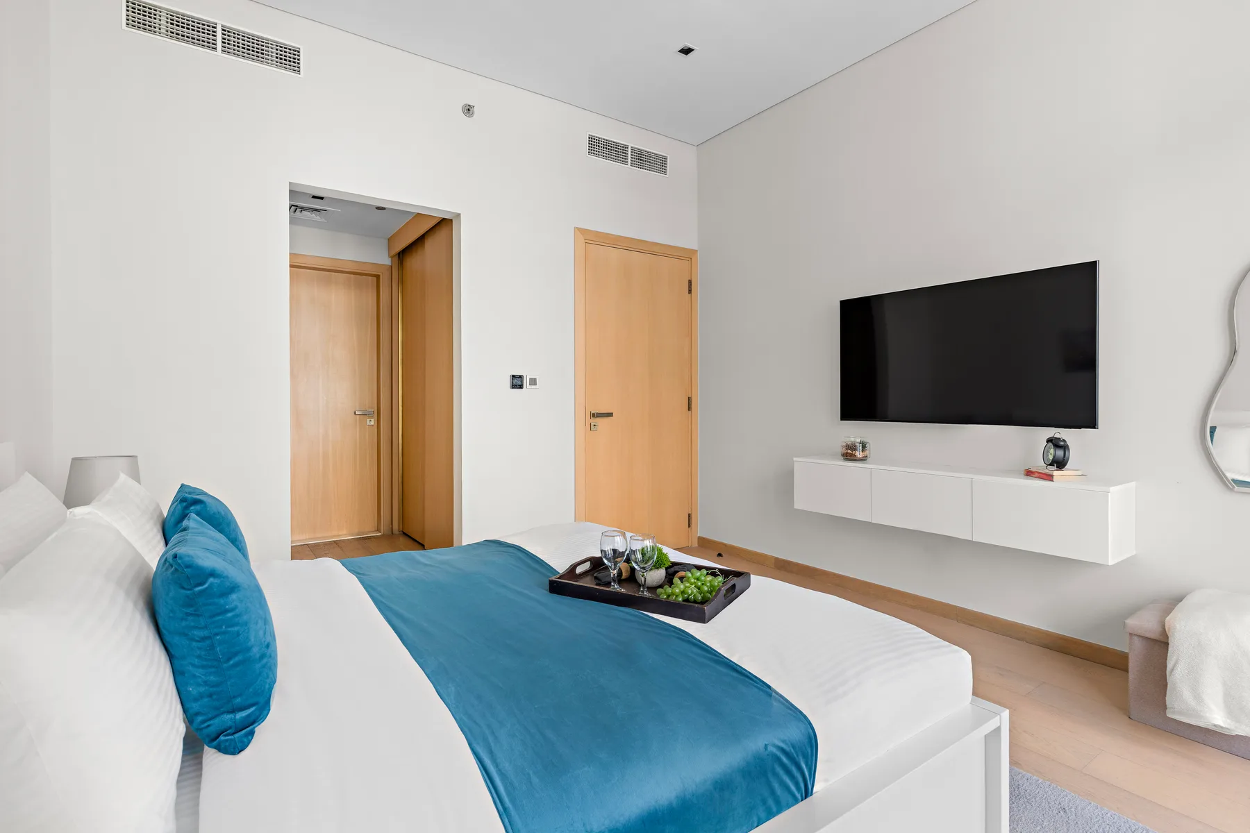 A bright bedroom with a neatly made bed and a wall-mounted television.