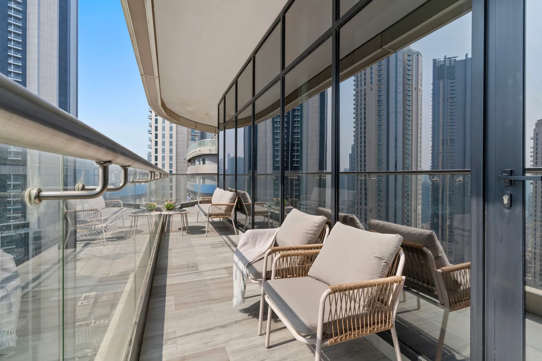 A balcony seating area with glass railings and views of nearby high-rise buildings.