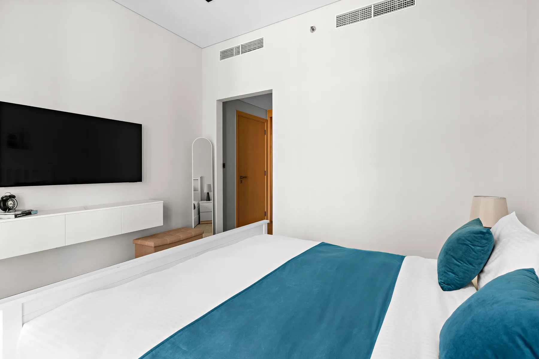 A bedroom with a white bed, teal bedding, and a wall-mounted television.