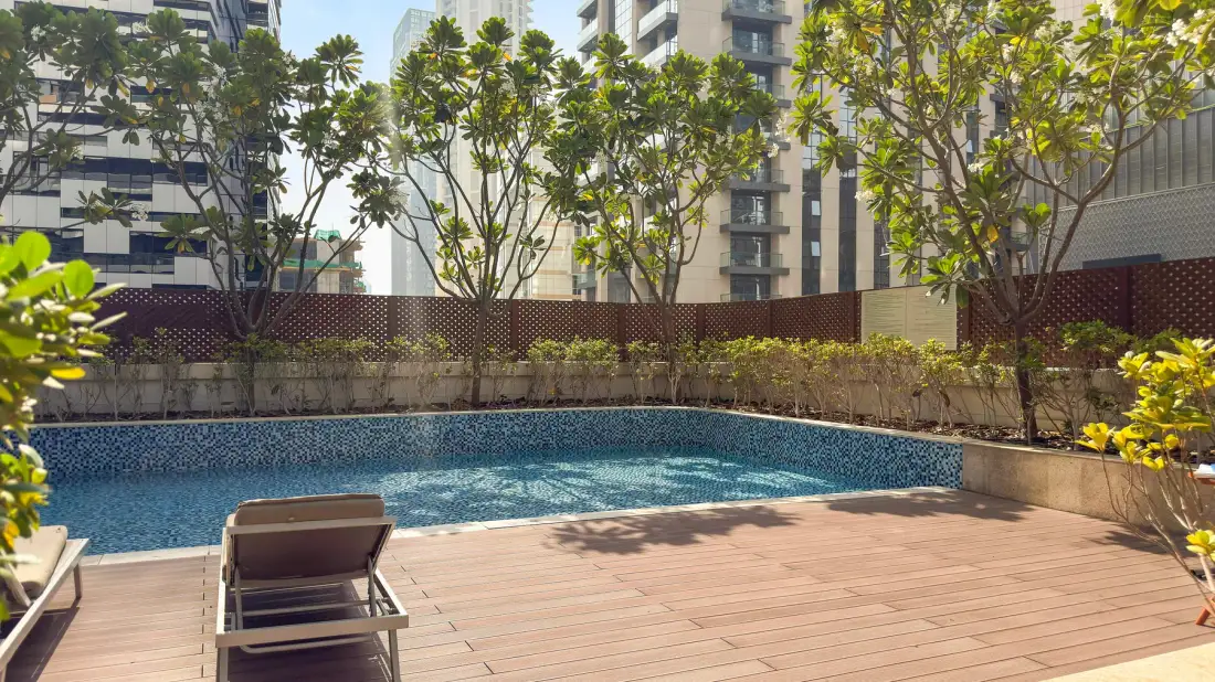 An outdoor swimming pool sits beside a wooden deck with seating and surrounding trees.